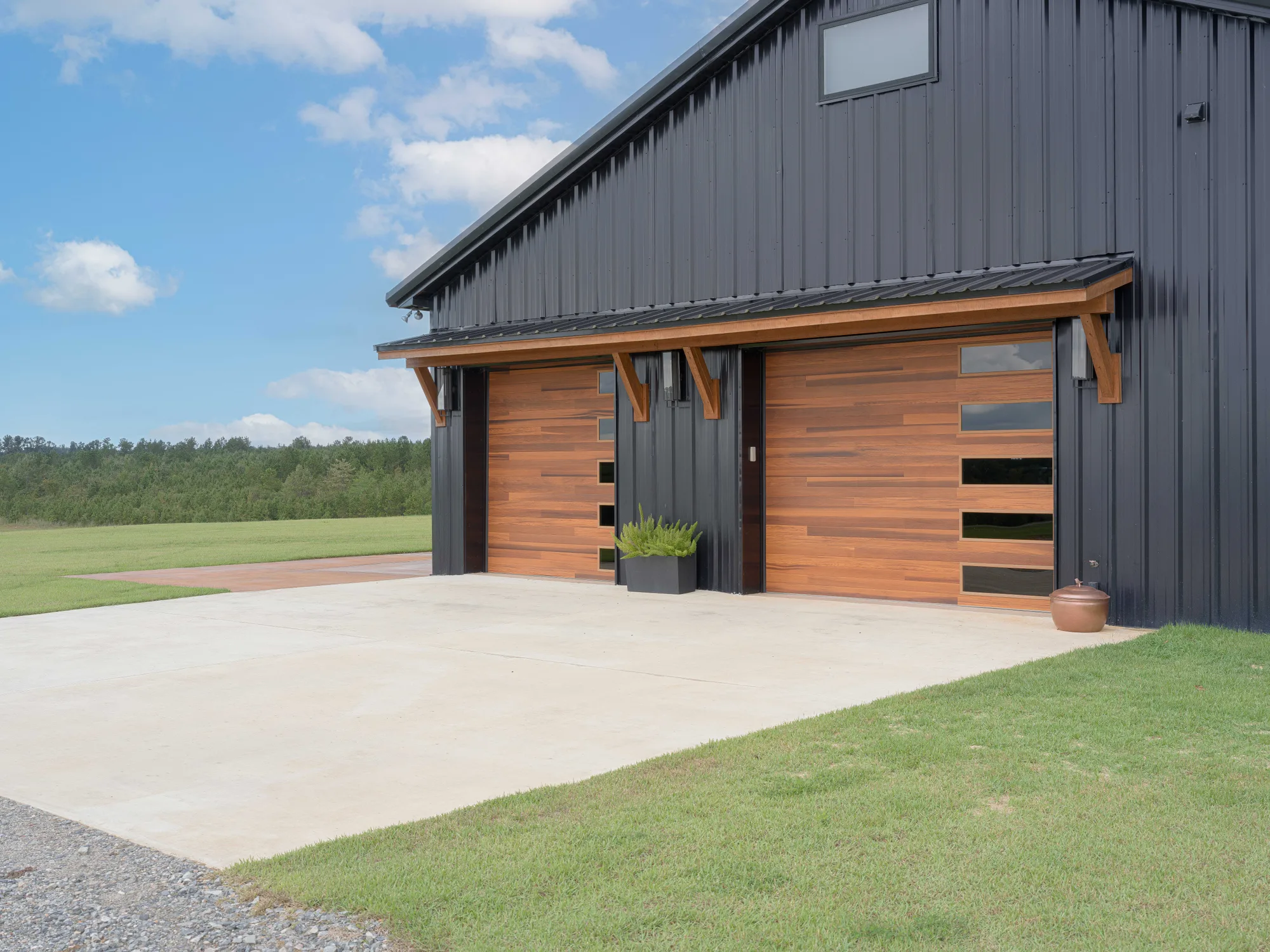Two cedar-tone horizontal plank garage doors with stacked side windows under a timber awning on a black metal building