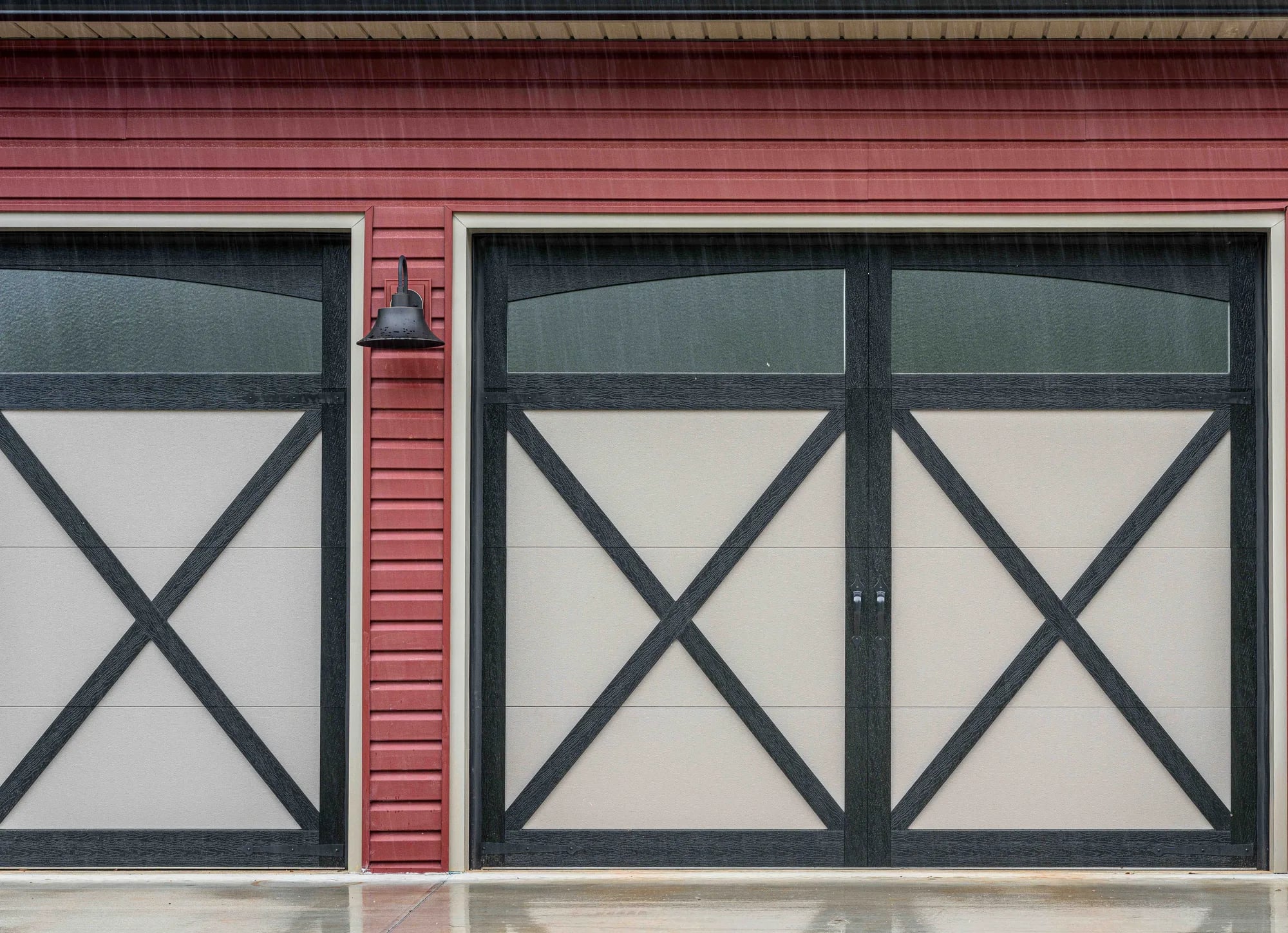 Black and tan overlay carriage-style garage doors with X-bracing and arched top glass on red siding