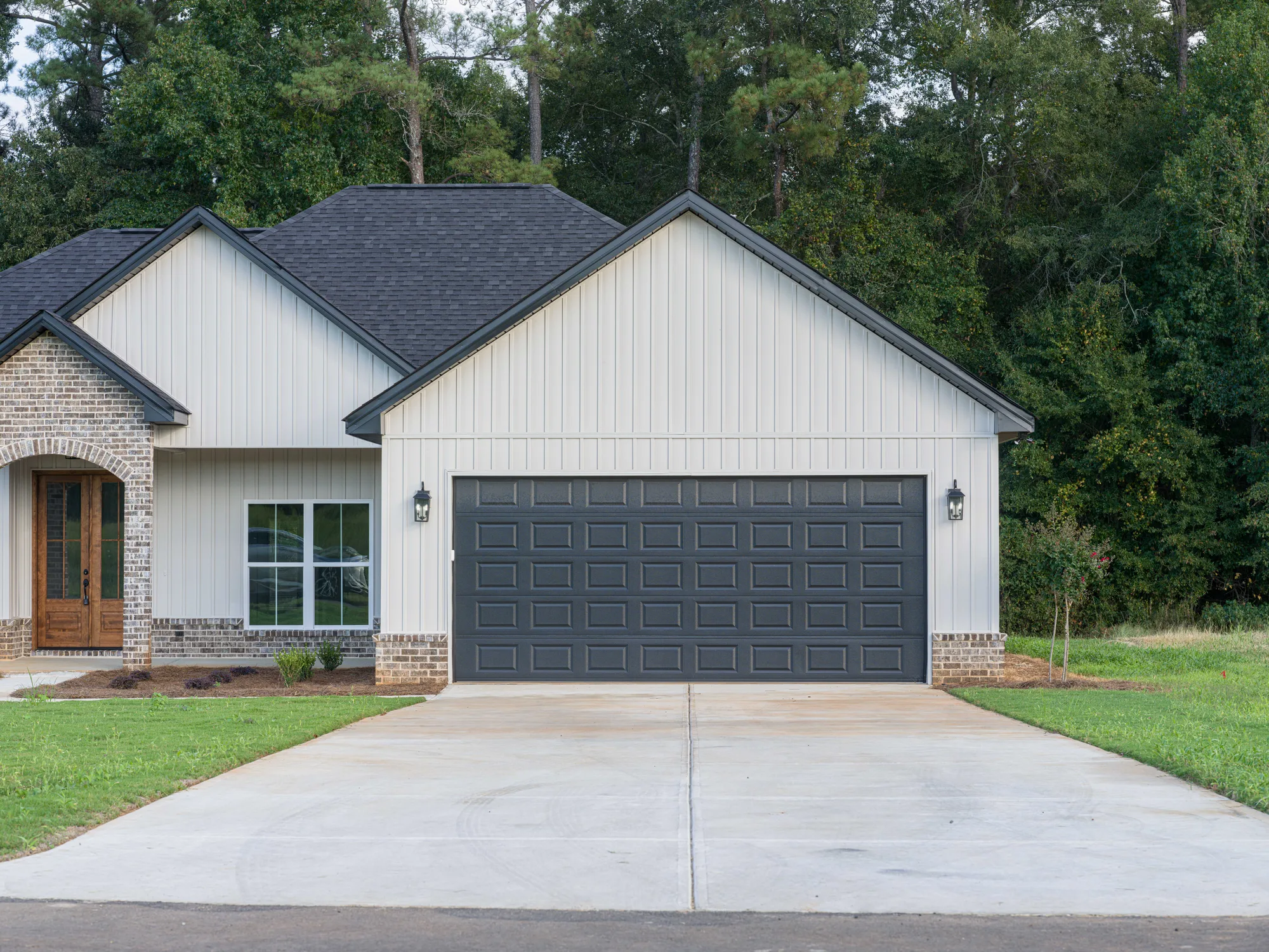 Charcoal raised-panel double garage door on an off-white board-and-batten home with brick accents