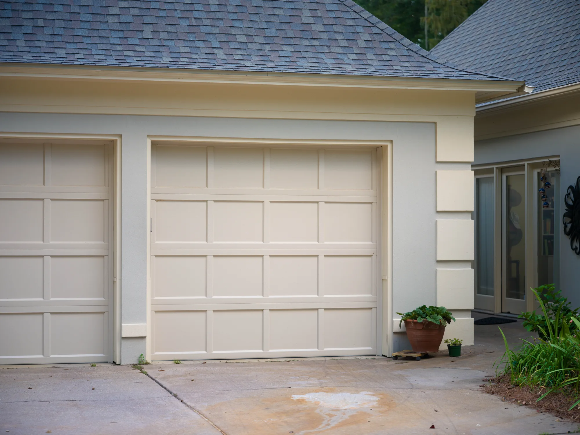 Cream recessed-panel garage doors on a cream stucco garage with a hip roof